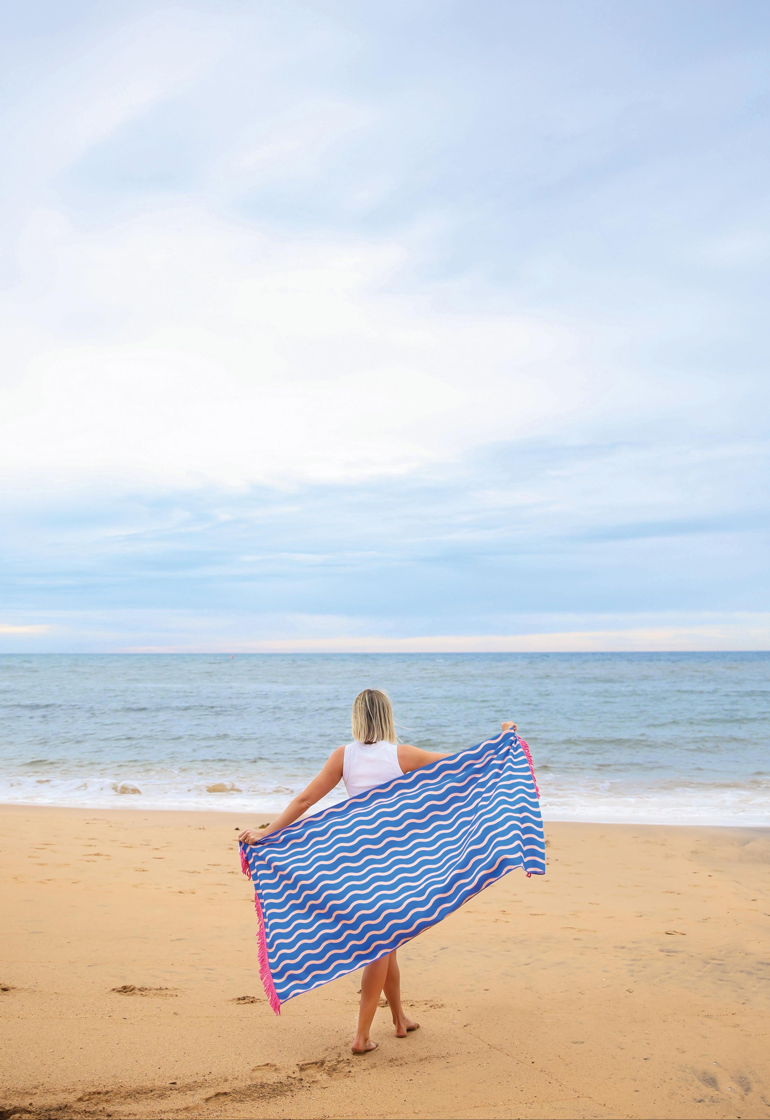 Person holding a blue and pink striped towel on a beach